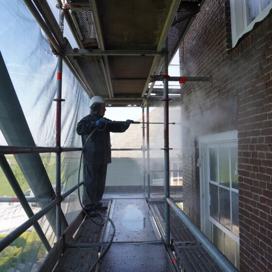 Een bouwvakker die met een hogedrukspuit de gevel van een rijksmonument aan het reinigen is