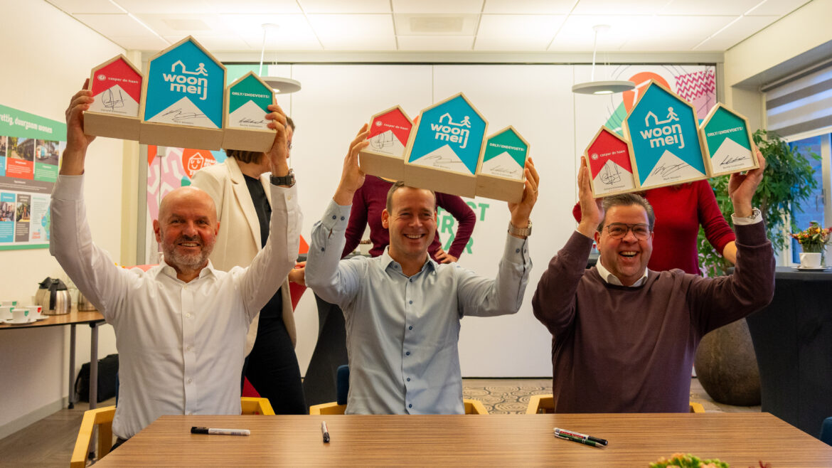 Berrie Endevoets van Orly & Endevoets, Mark Wonders van Woonmeij en Gerard Dinnessen van Caspar de Haan houden houten huisjes omhoog met daarop hen handtekening. Dit symboliseert de ondertekening van het handboek verduurzaming.