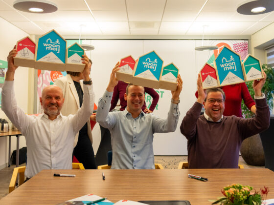 Berrie Endevoets van Orly & Endevoets, Mark Wonders van Woonmeij en Gerard Dinnessen van Caspar de Haan houden houten huisjes omhoog met daarop hen handtekening. Dit symboliseert de ondertekening van het handboek verduurzaming.